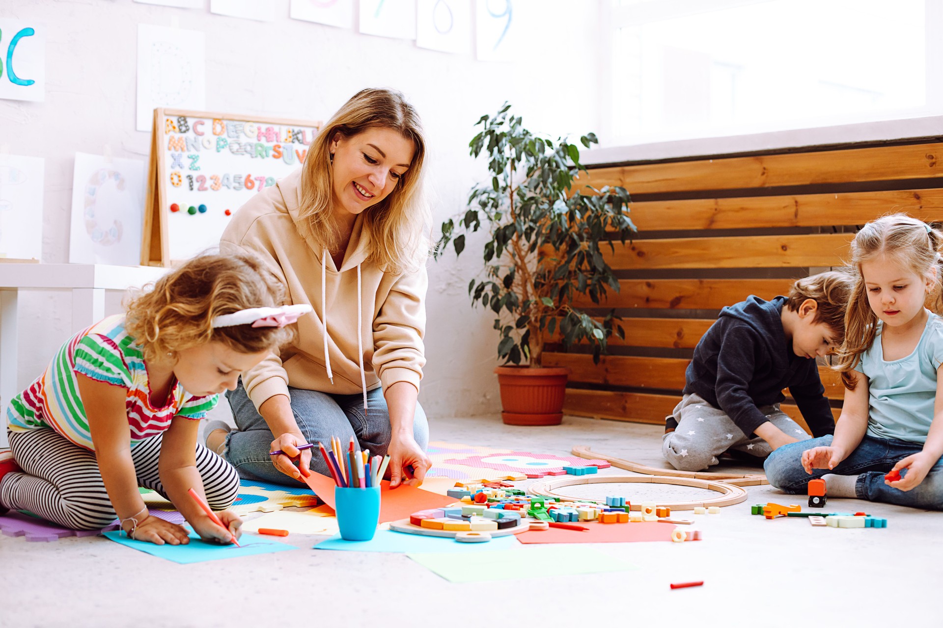 Portrait of young smiling woman teacher sitting with wonderful children, checking looking at painting on red paper.